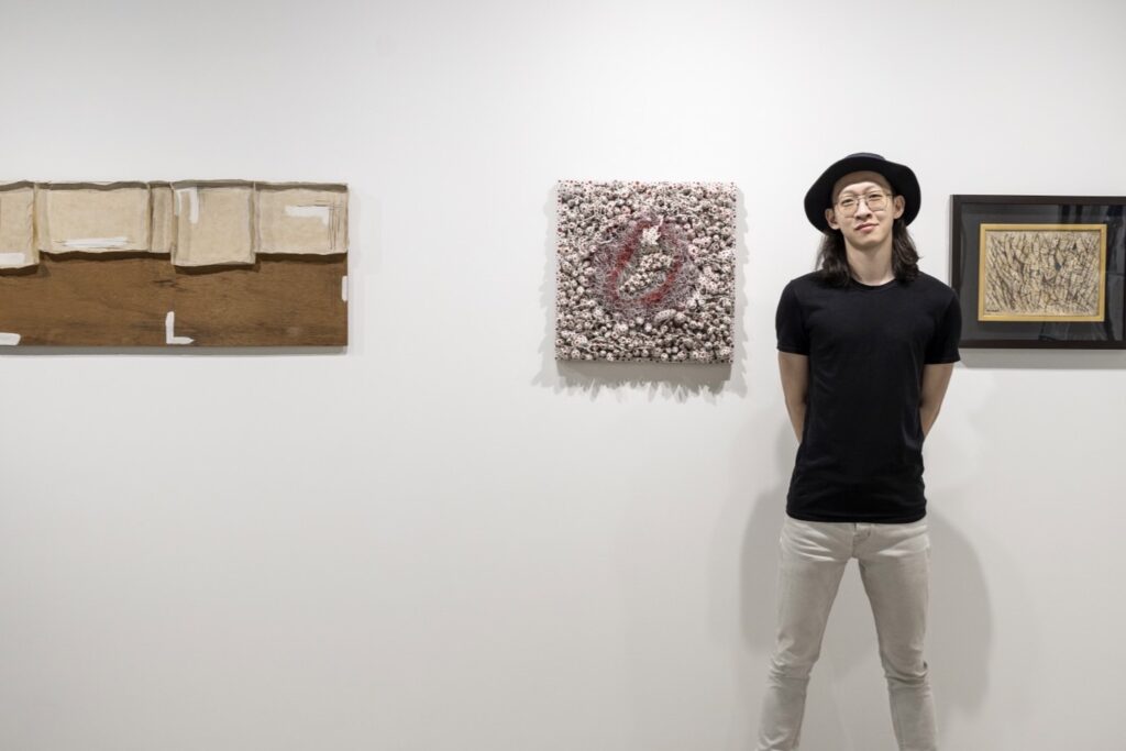 謝亞修身後是展覽《V｜Chapter I》的三幅作品（由左至右：菅木志雄的《無界》，草間彌生的《A Grape》，難波田龍起的《集合》），由台灣藏家提供。（謝亞修提供）